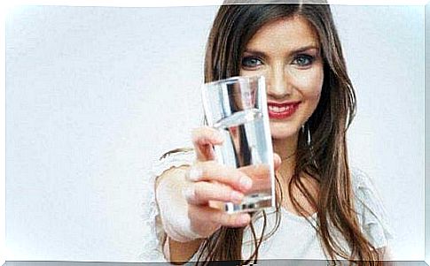 A woman is holding a glass of water with an outstretched hand.