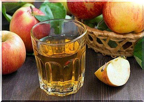 A glass of apple water with some apples next to it.